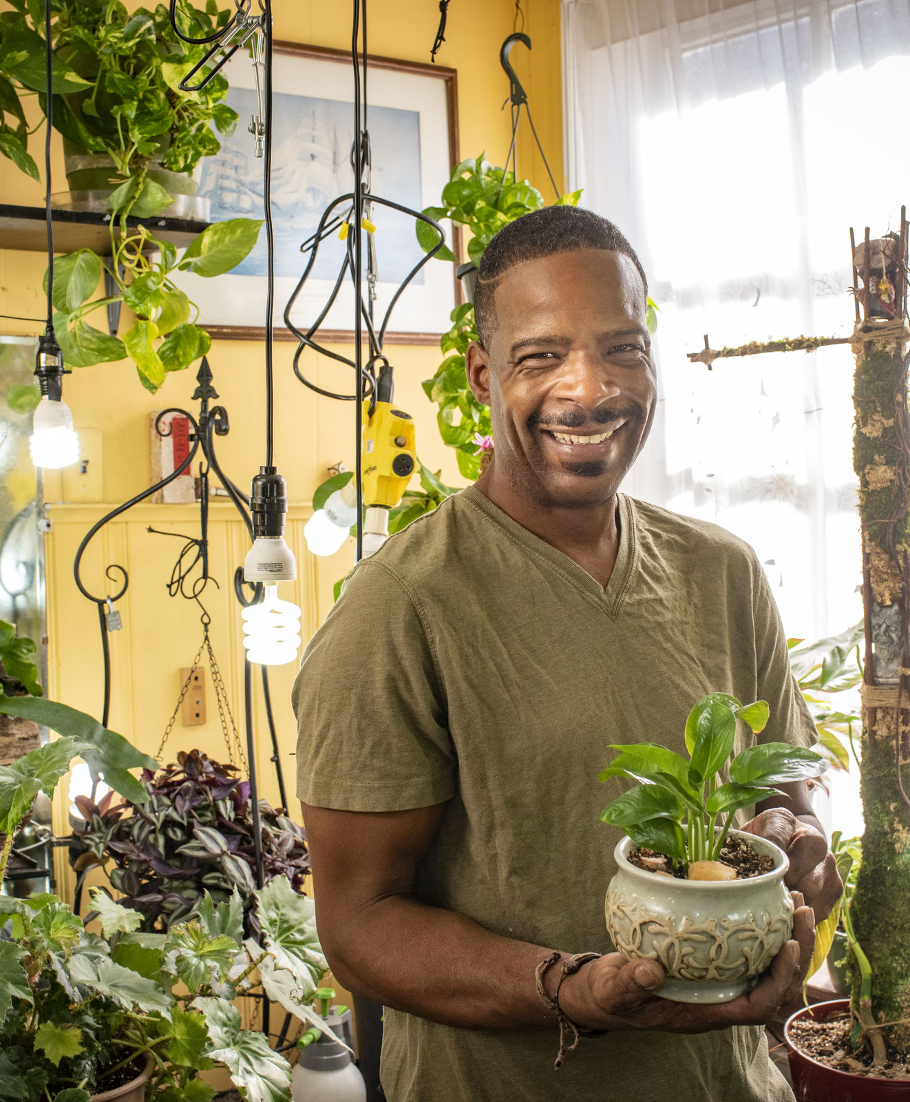 Man indoors holding a potted plants among many potted plants